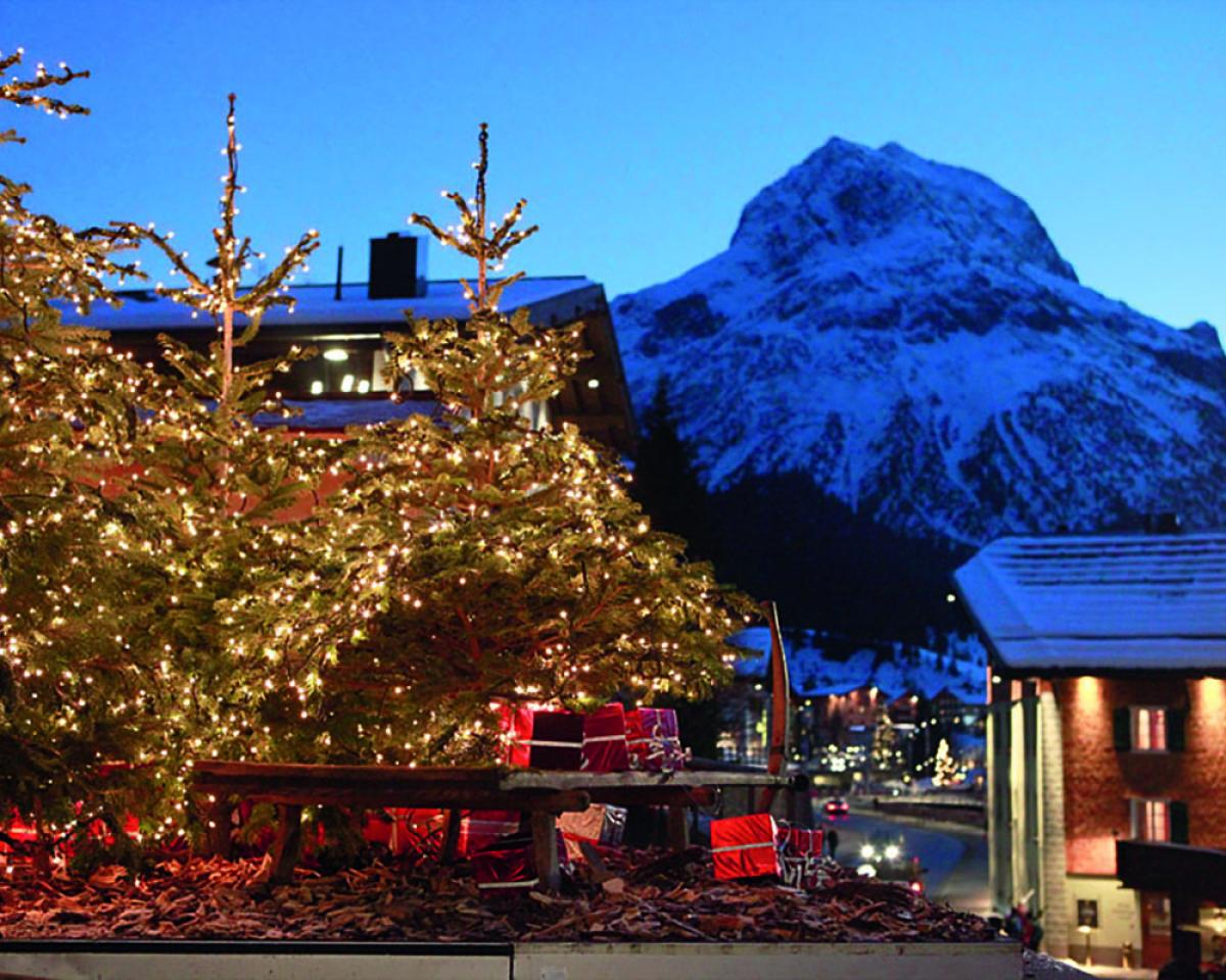 Guests enjoying drinks on the terrace at Hotel Post Lech with snowy mountains in background