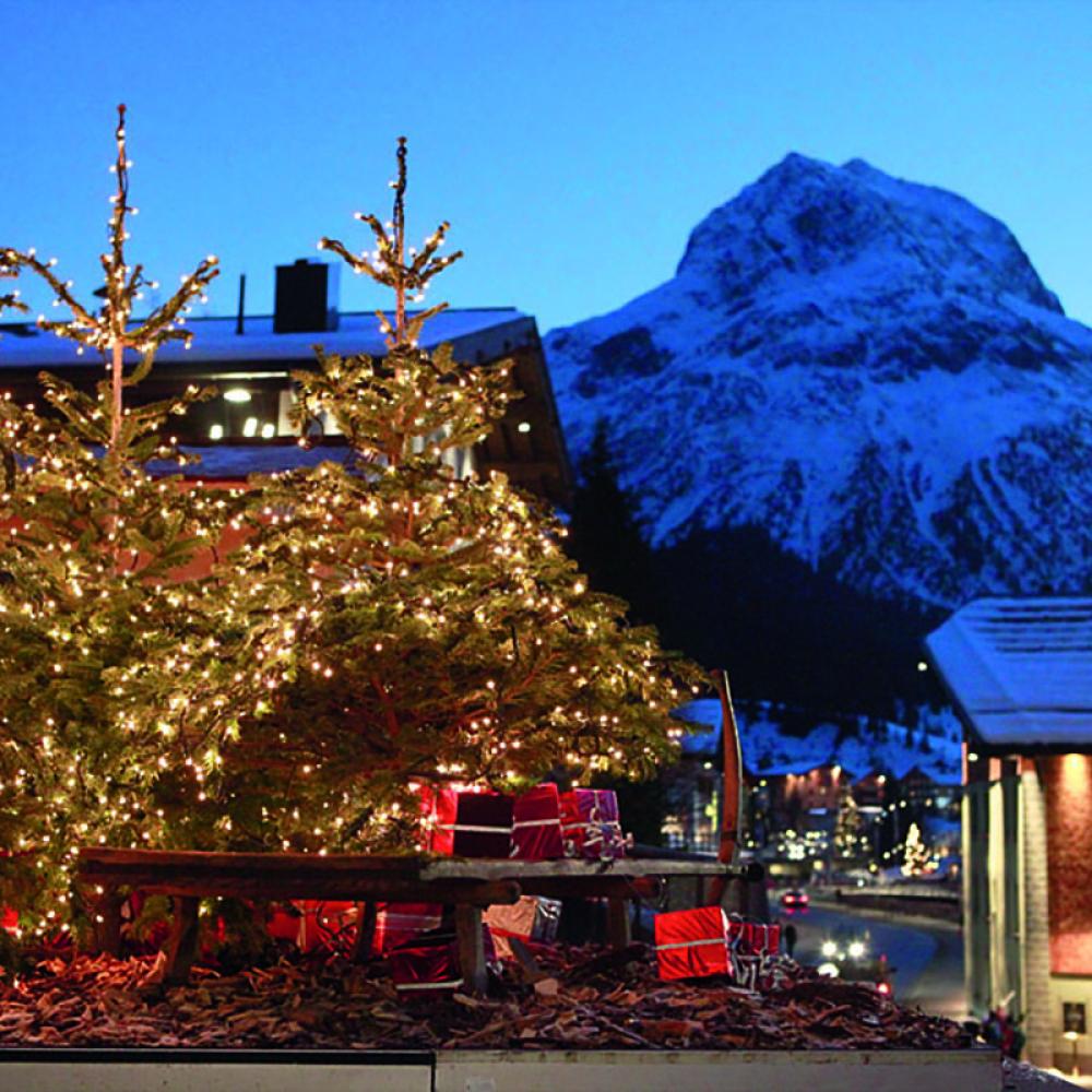 Guests enjoying drinks on the terrace at Hotel Post Lech with snowy mountains in background