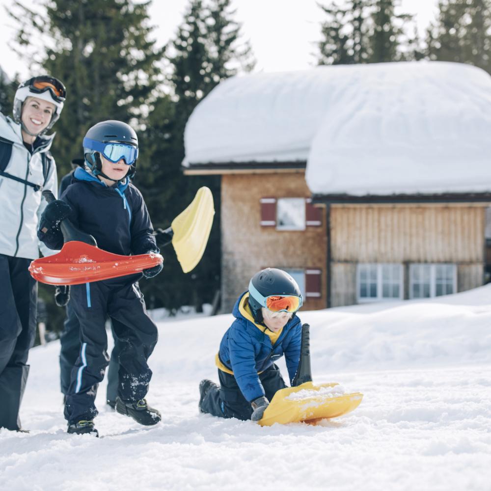 Three people sledding in the snow outside a hut – Hotel Post Lech