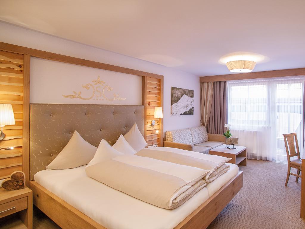 Schlafzimmer im Hotel Salnerhof mit großem Bett, Holzvertäfelung und hellen Vorhängen