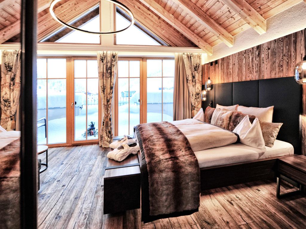 Schlafzimmer im Hotel Salnerhof mit großem Bett, Holzbalkendecke und hohen Fenstern