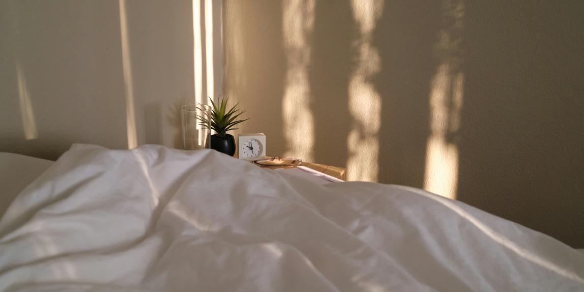 Weiches Bett mit weißer Bettwäsche und Glockna-Wecker auf Nachttisch