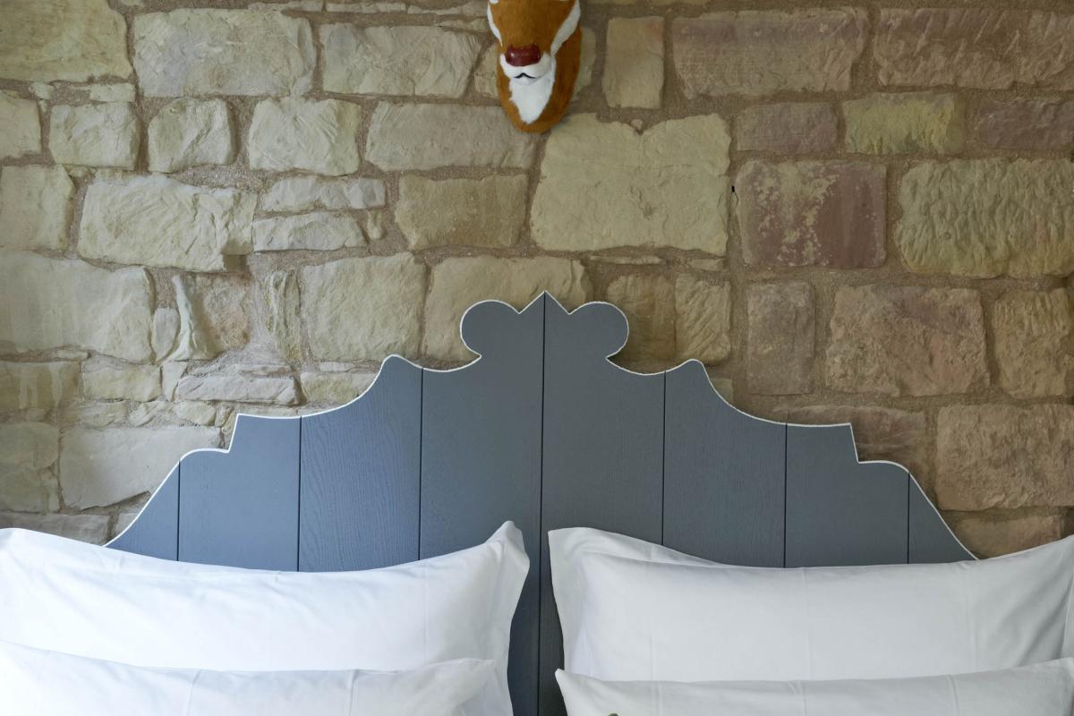 Bett mit Lösch-kissen vor Steinwand und Hirschkopf-Deko