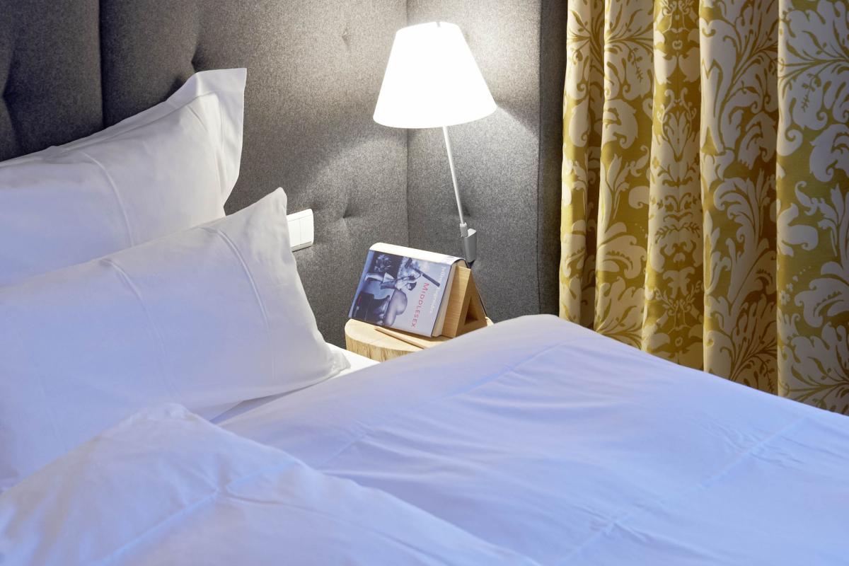 Hell beleuchtetes Schlafzimmer mit Lösch-Lampe neben grau gepolstertem Kopfteil