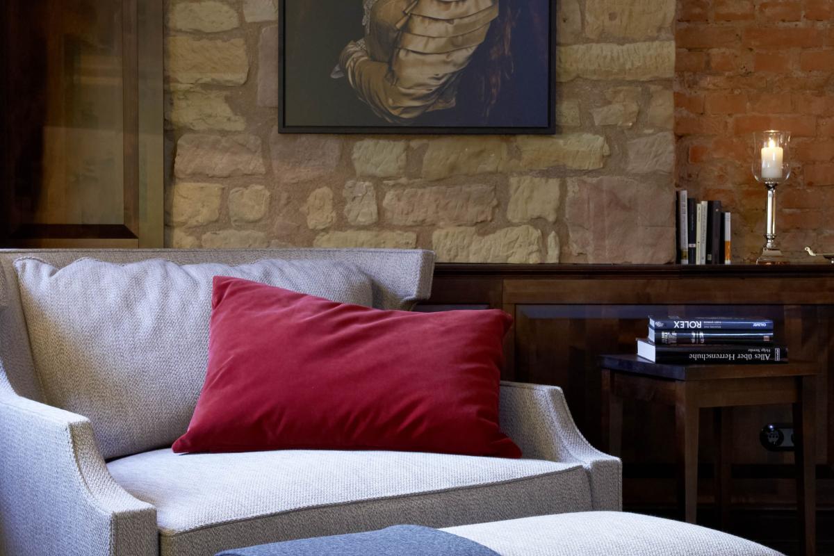 Gemütliches Wohnzimmer mit grauem Sofa, rotem Kissen und Lösch-Bild an Steinwand