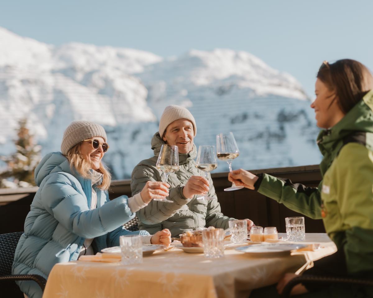Guests enjoying drinks on the terrace at Hotel Post Lech with snowy mountains in background