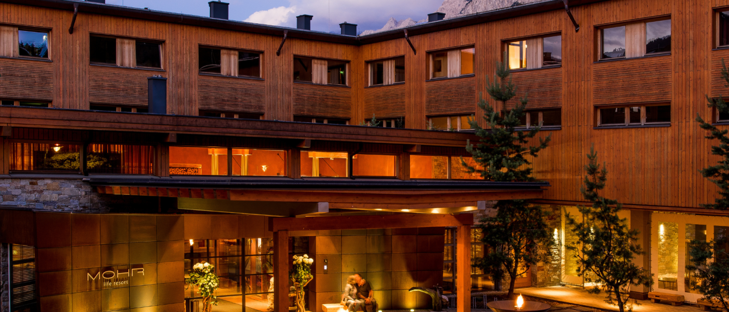 Außenansicht des beleuchteten Hotel MOHR life resort am Abend mit Bergkulisse.