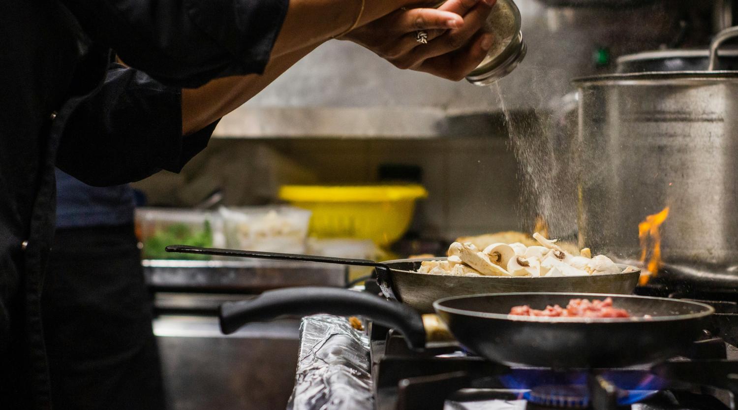 Glockna chef seasoning mushrooms in a pan on gas stove in professional kitchen