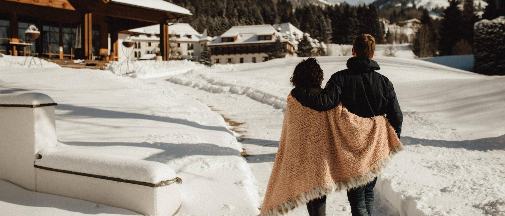 Coppia nella neve davanti allo Schlosshotel Kitzbühel, con le montagne sullo sfondo