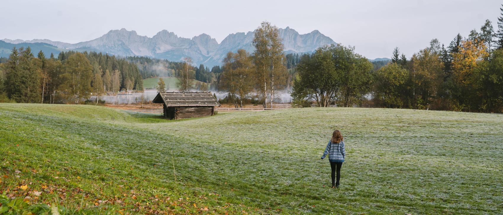 Person walking across a meadow with the Alps beyond, near Schlosshotel Kitzbühel