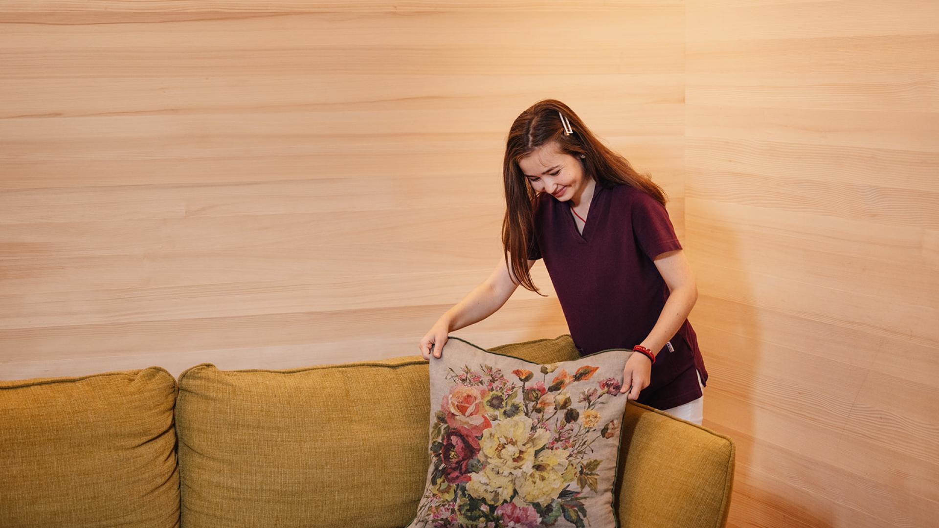 Hotel Aurora Mitarbeiterin richtet Sofakissen mit Blumenmuster her