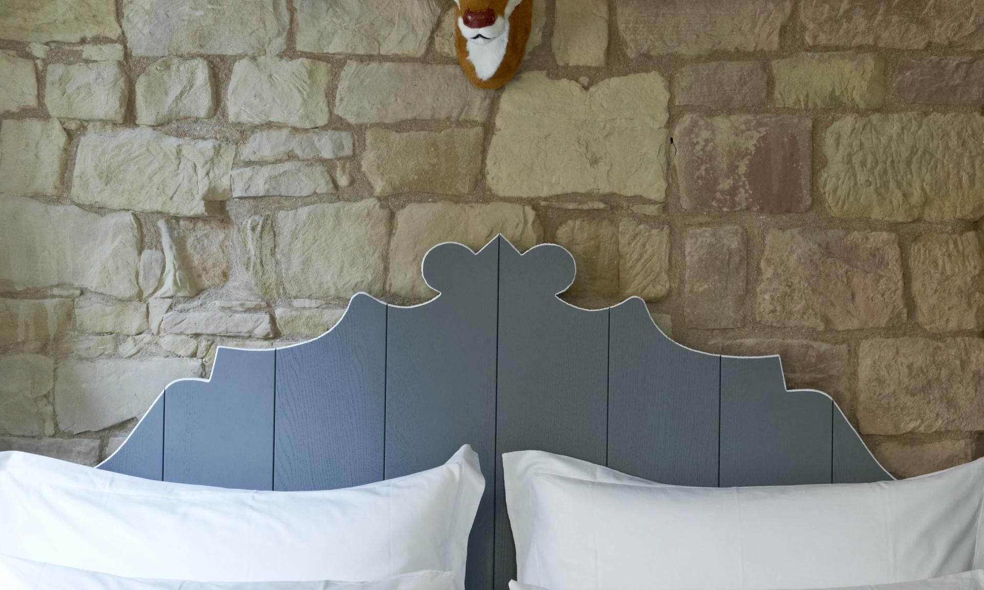 Bett mit Lösch-kissen vor Steinwand und Hirschkopf-Deko