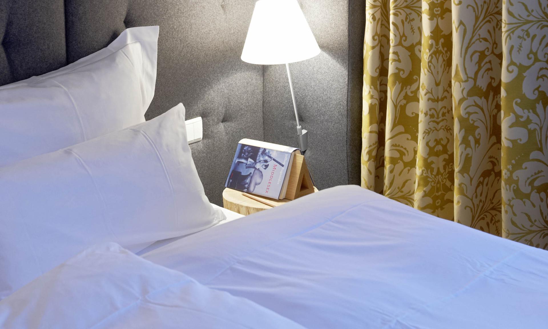 Hell beleuchtetes Schlafzimmer mit Lösch-Lampe neben grau gepolstertem Kopfteil