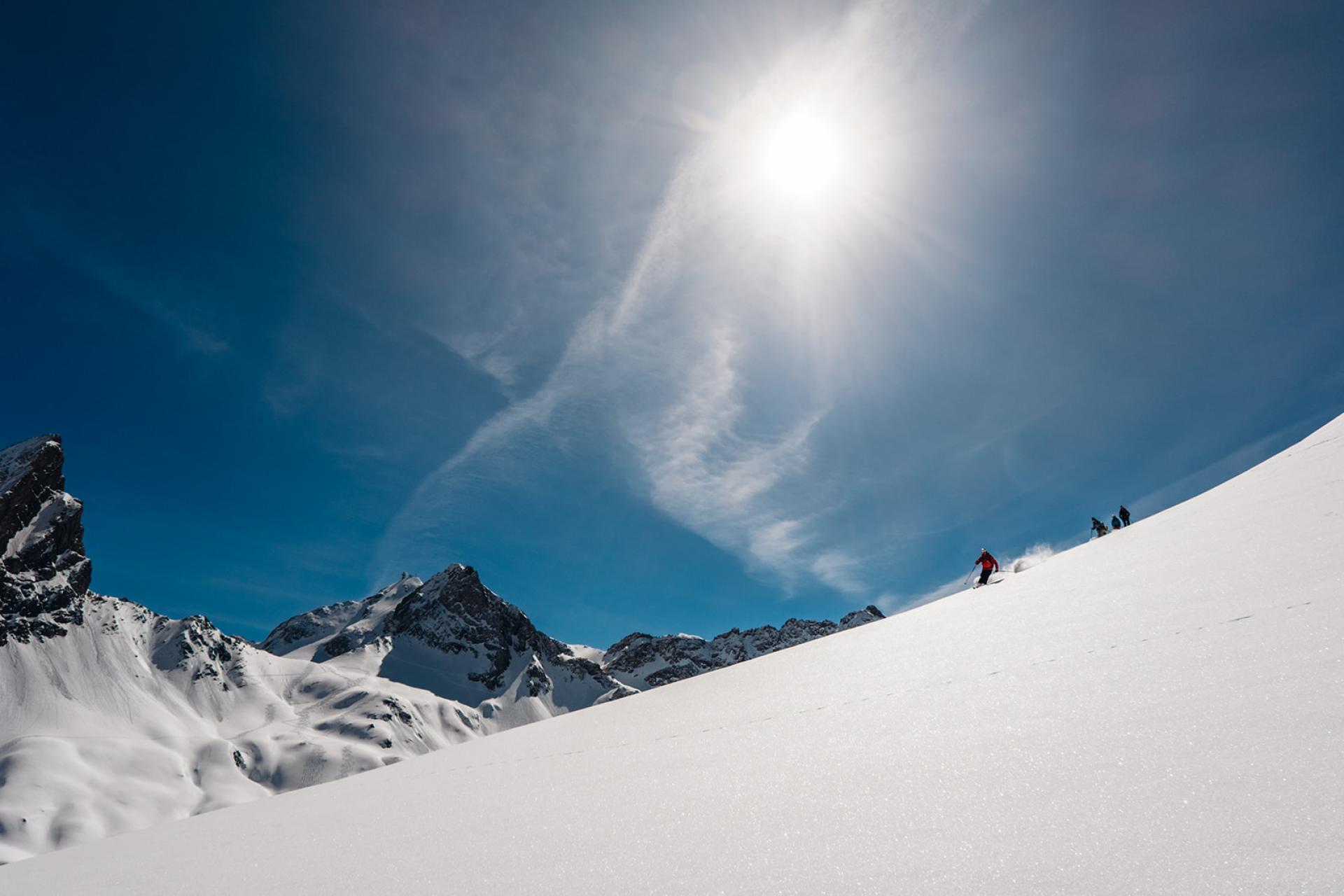 Ski fahren im Sonnenschein auf verschneitem Hang mit Hotel Aurora im Hintergrund