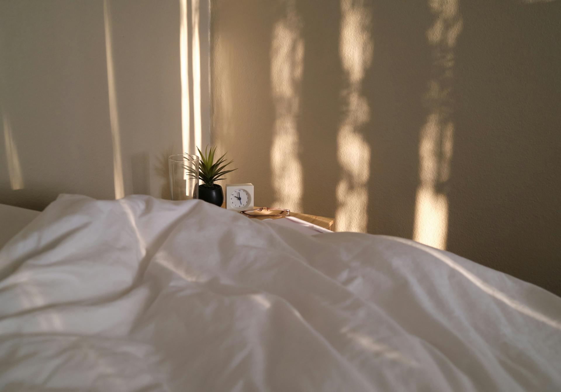 Weiches Bett mit weißer Bettwäsche und Glockna-Wecker auf Nachttisch
