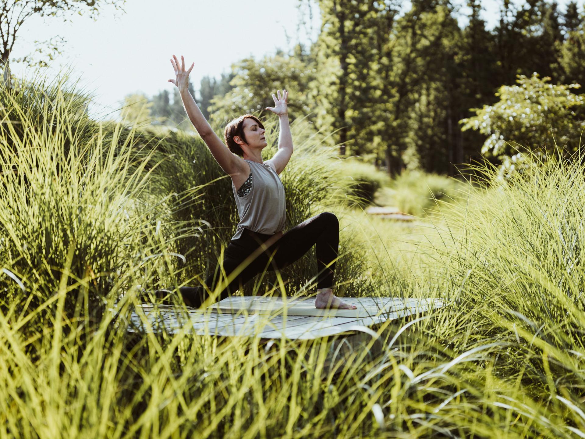 Frau macht Yoga im Freien im Seezeitlodge Hotel & Spa umgeben von grüner Natur