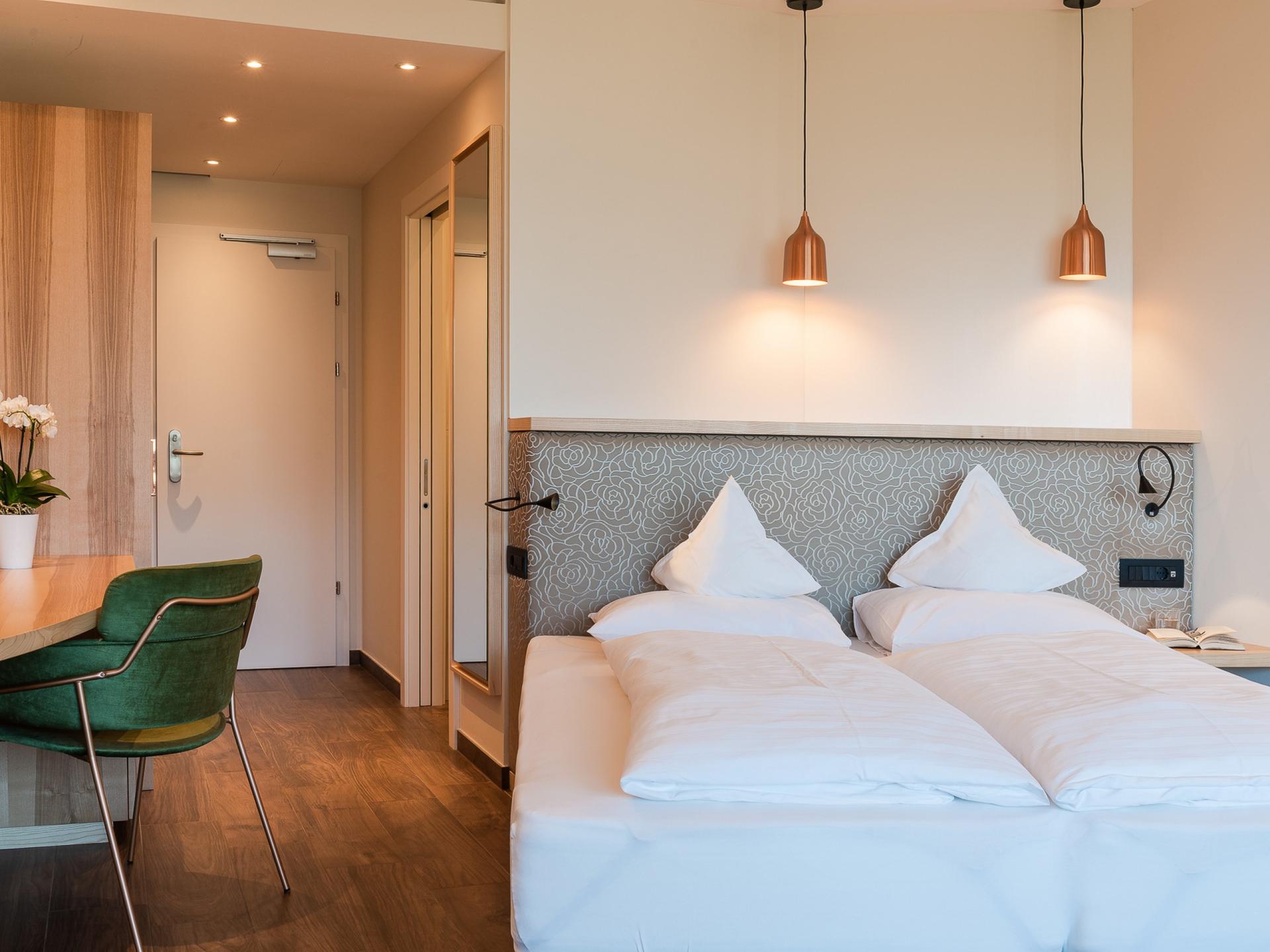 Modernes Doppelzimmer im Alpenpalais Kröll mit grünem Stuhl und Holzboden