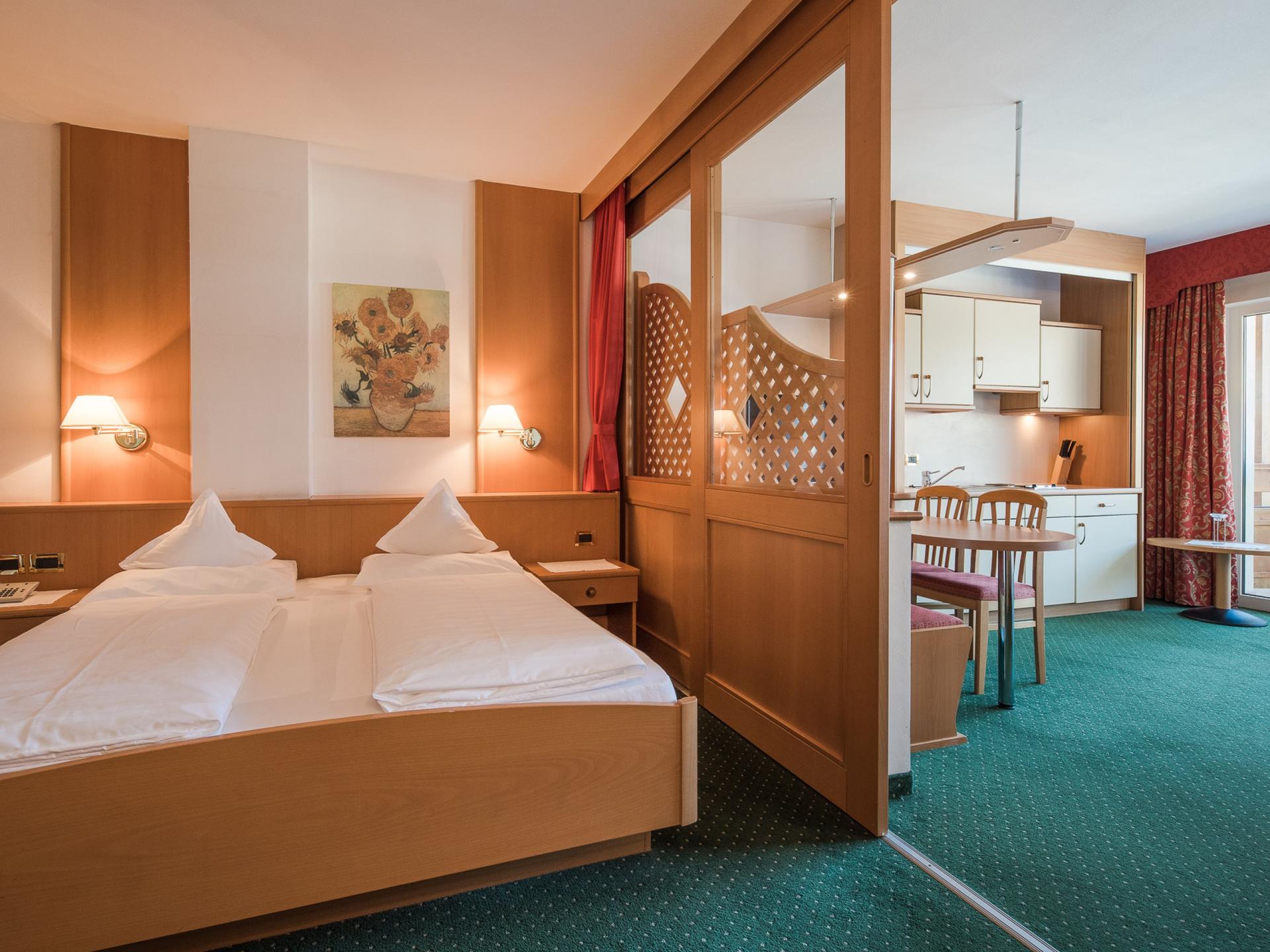 Zimmer im Alpenpalais Kröll mit Bett und Blick auf Küchenbereich