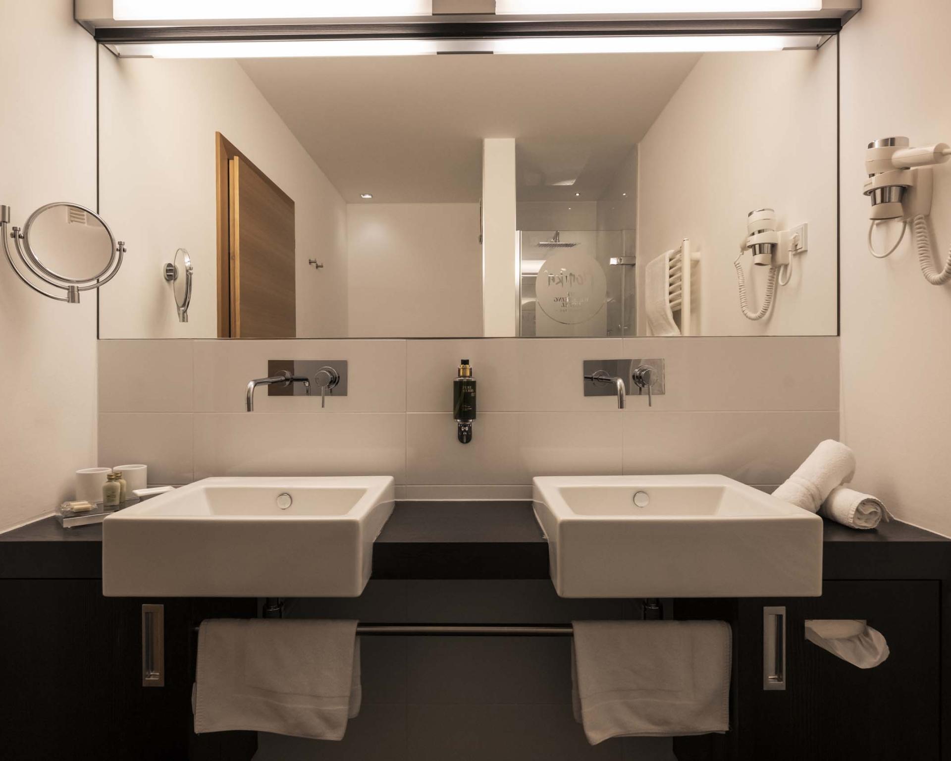 Hotel Monika Badezimmer mit Doppelwaschbecken, Handtüchern und Wandföhn