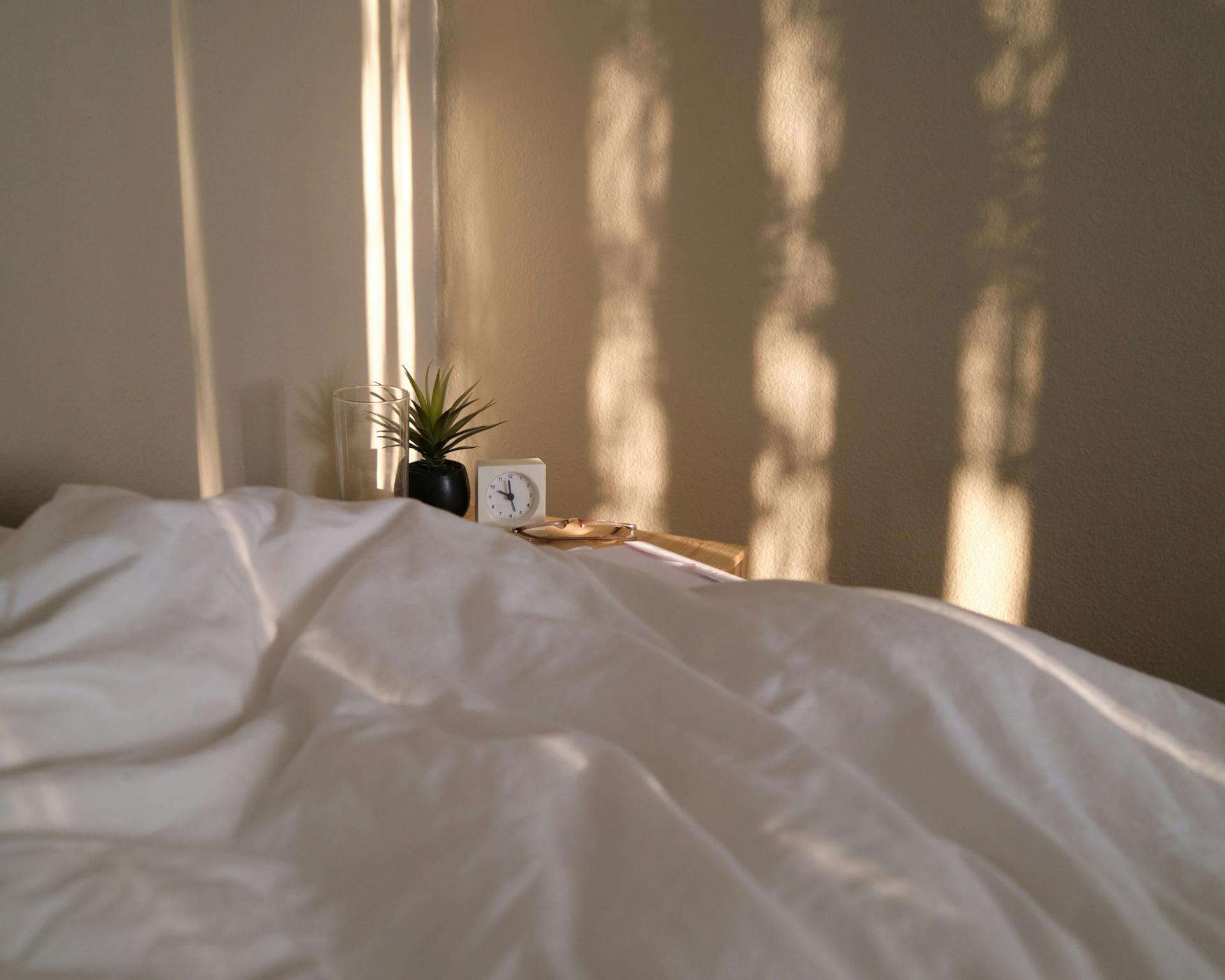 Weiches Bett mit weißer Bettwäsche und Glockna-Wecker auf Nachttisch