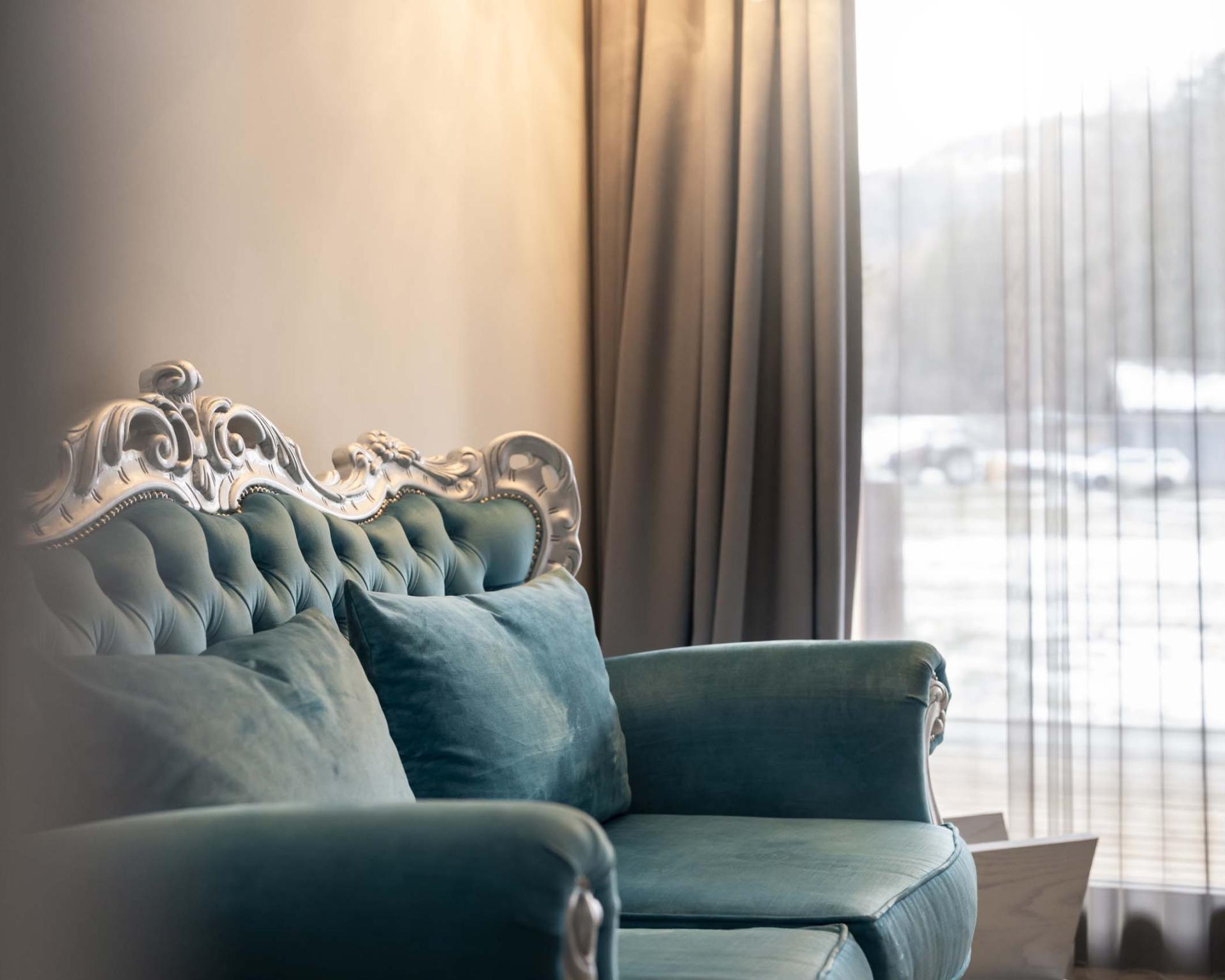 Elegantes grünes Sofa im Zimmer des Hotel Monika vor Vorhängen und Fenster