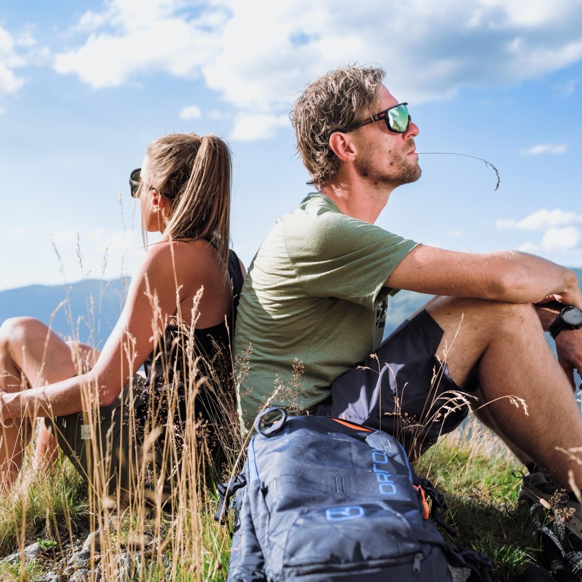Paar sitzt mit Rucksack in der Natur und blickt auf die Gipfel der Hohen Tauern