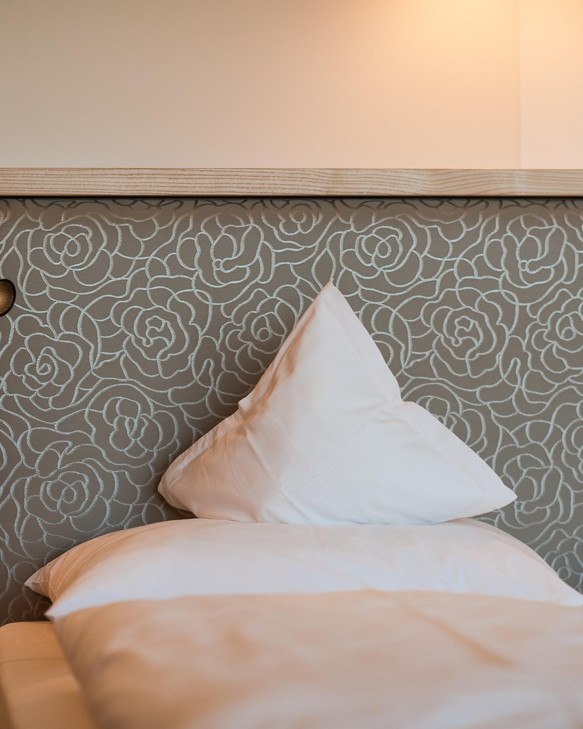 Gemütliches Bett im Alpenpalais Kröll mit floralem Polsterkopfteil