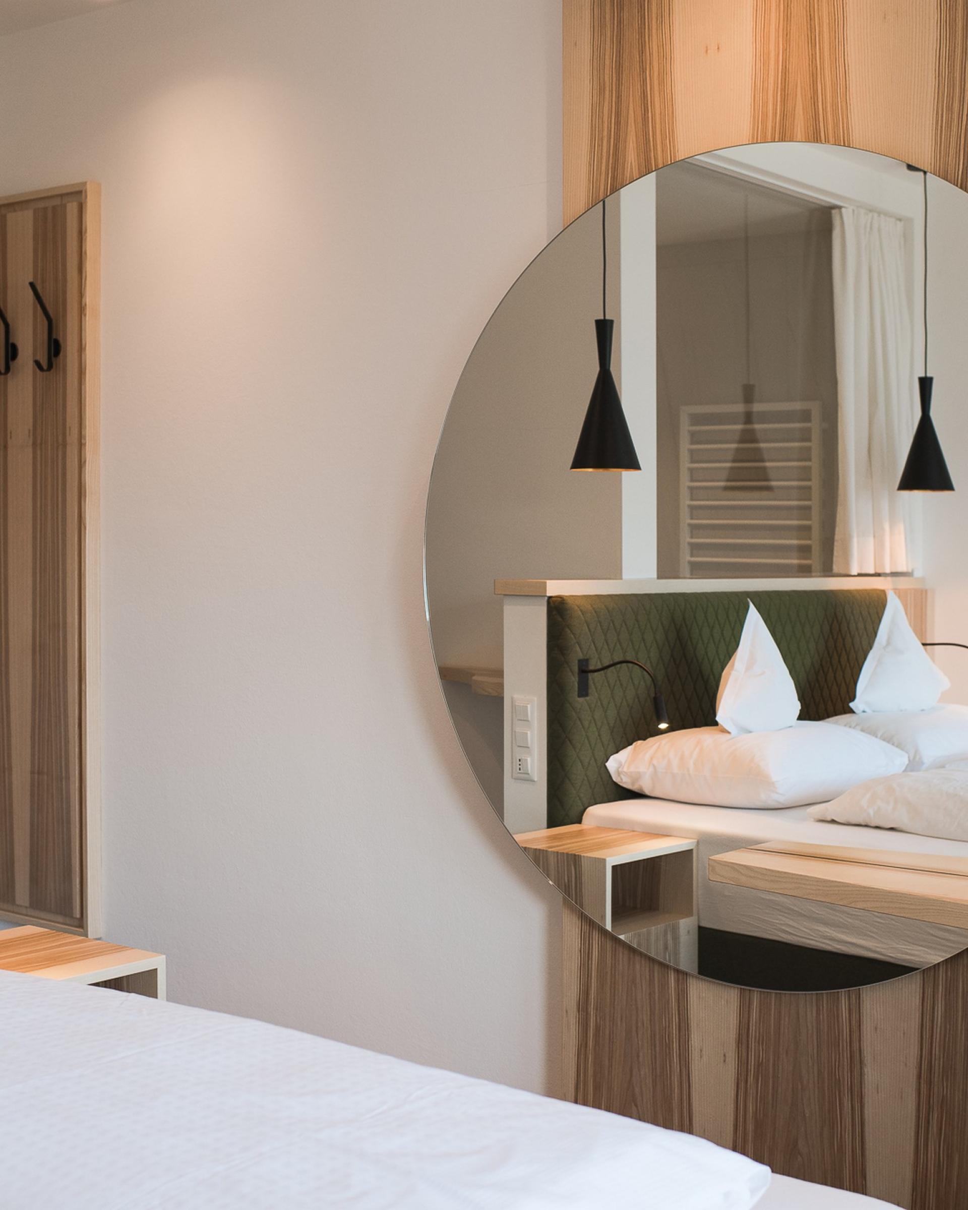 Modernes Zimmer im Alpenpalais Kröll mit rundem Spiegel und Bett