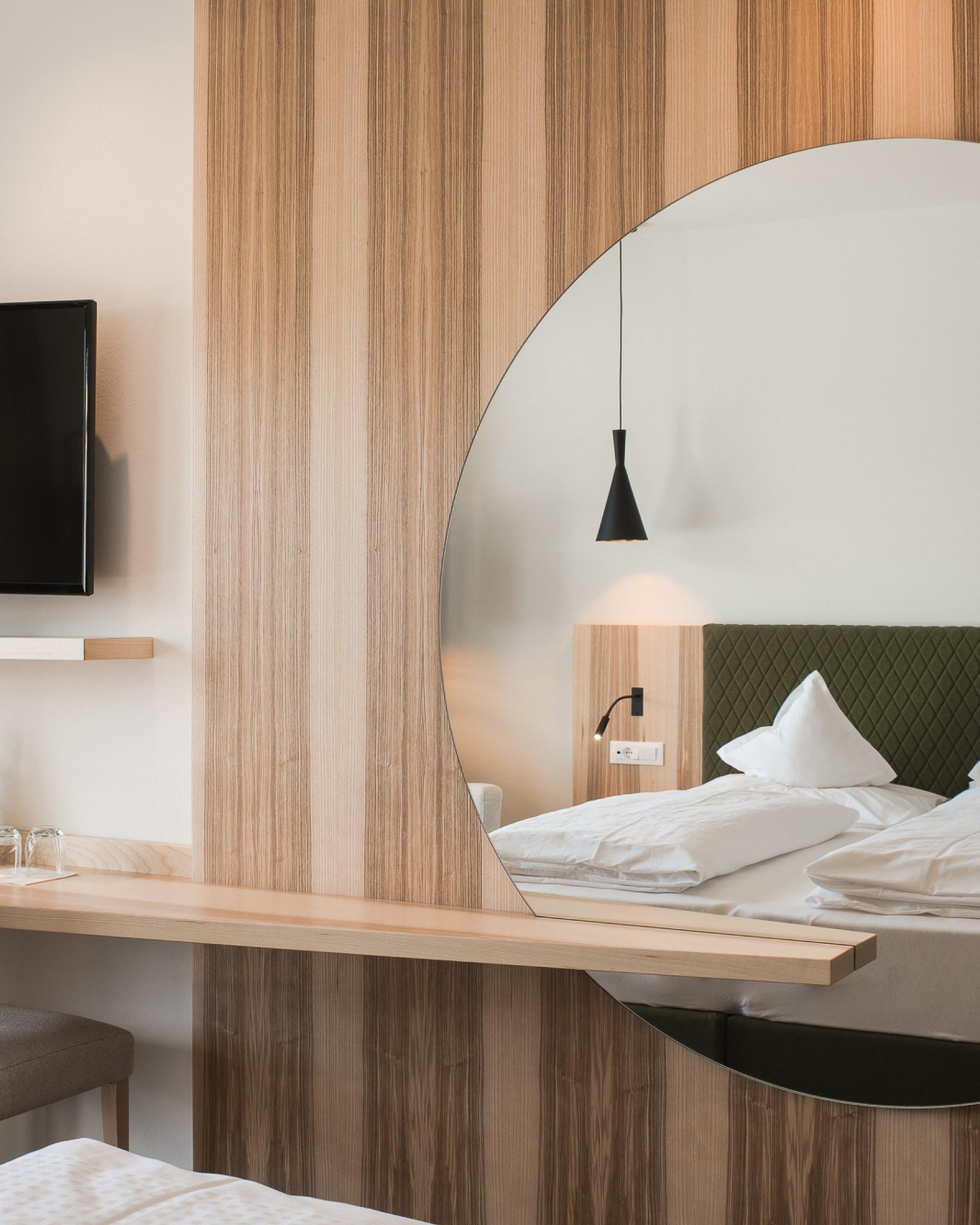 Modernes Hotelzimmer im Alpenpalais Kröll mit Holzvertäfelung und rundem Spiegel