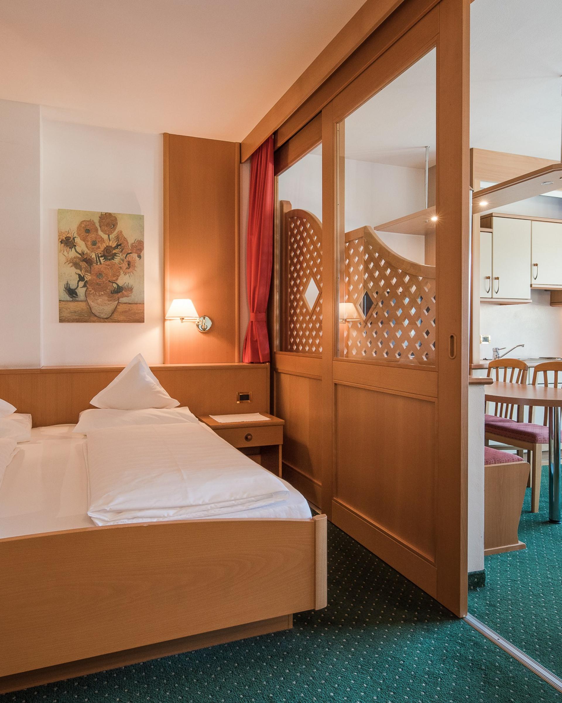 Zimmer im Alpenpalais Kröll mit Bett und Blick auf Küchenbereich