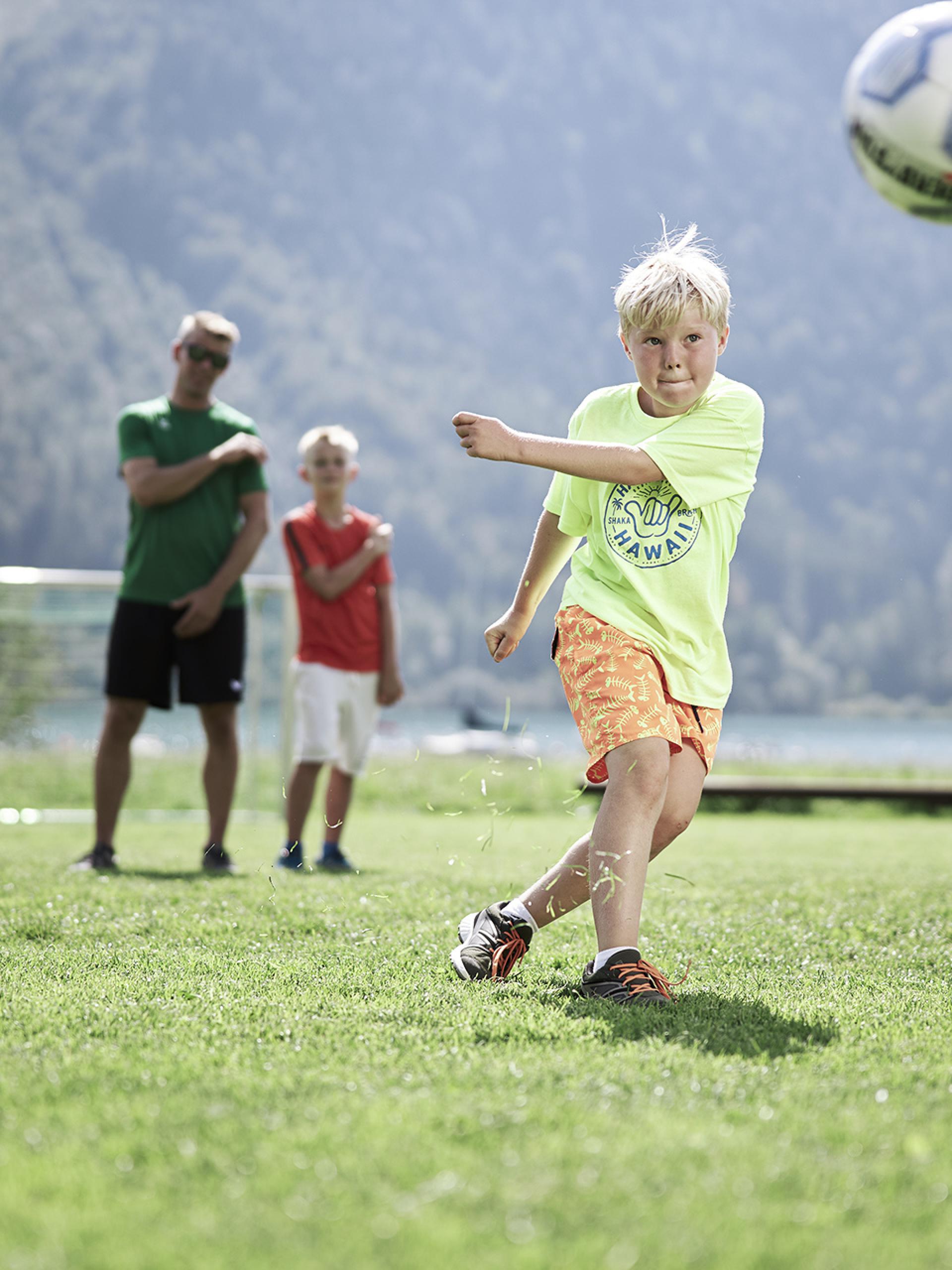 Child playing soccer at Familienresort Buchau with mountain backdrop