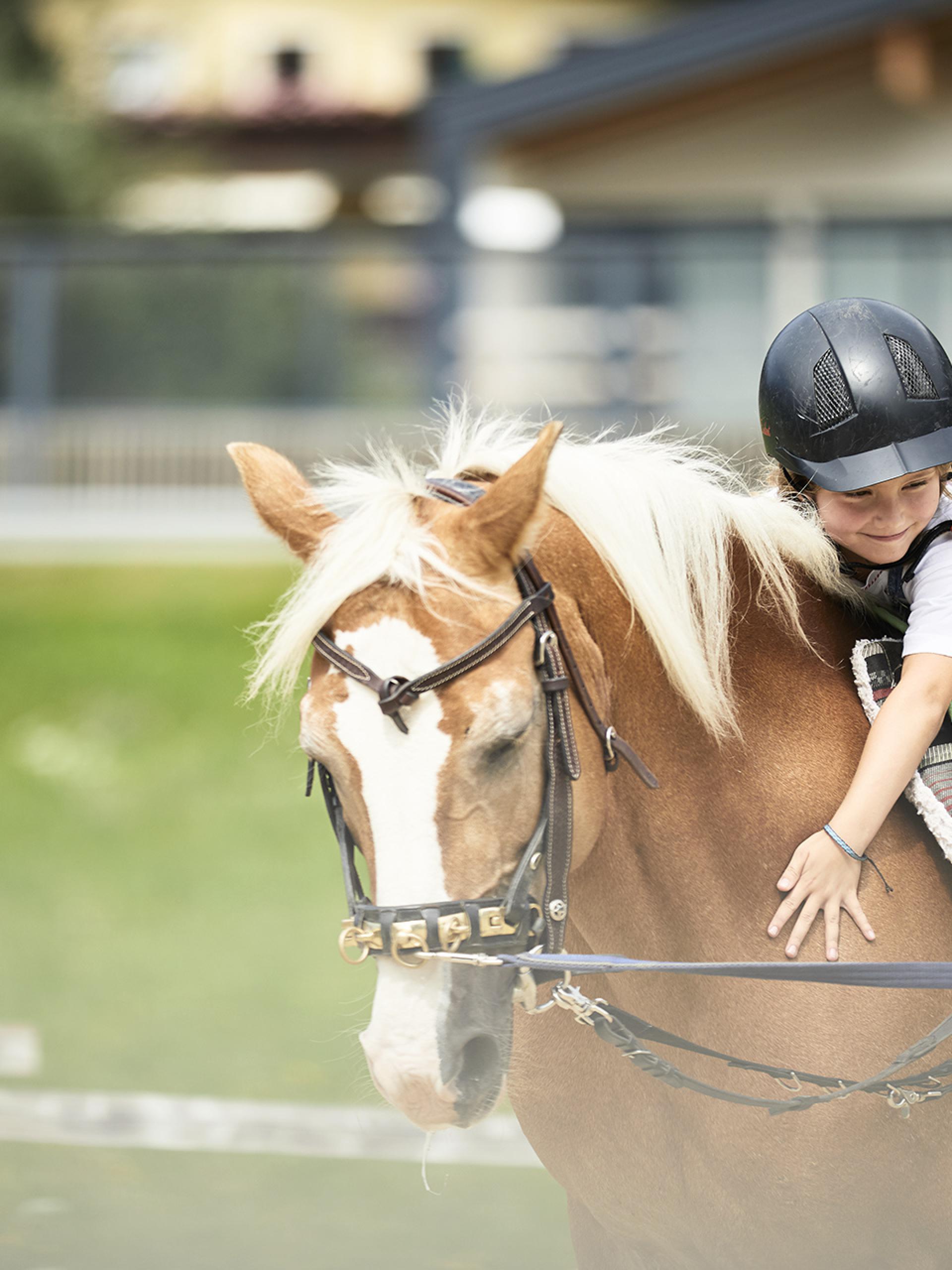 Child riding horse happily at Familienresort Buchau wearing helmet
