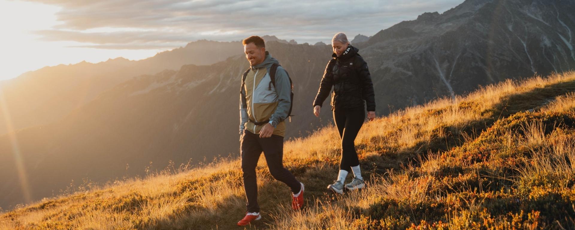 Hotel Gassner **** Superior Gäste wandern auf sonnenbeschienener Bergwiese mit Alpen im Hintergrund