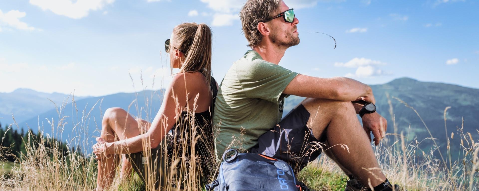 Paar sitzt mit Rucksack in der Natur und blickt auf die Gipfel der Hohen Tauern