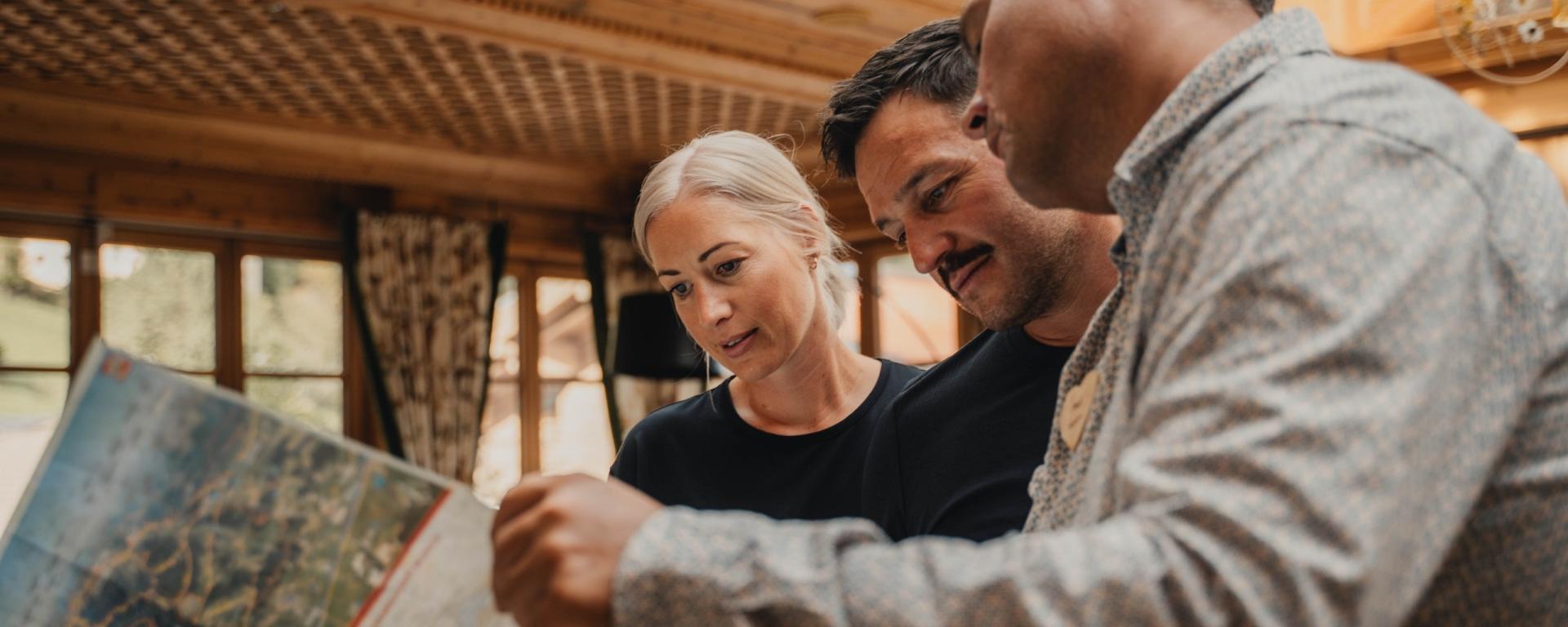 Gäste im Hotel Gassner **** Superior studieren zusammen eine Karte in gemütlichem Holzambiente