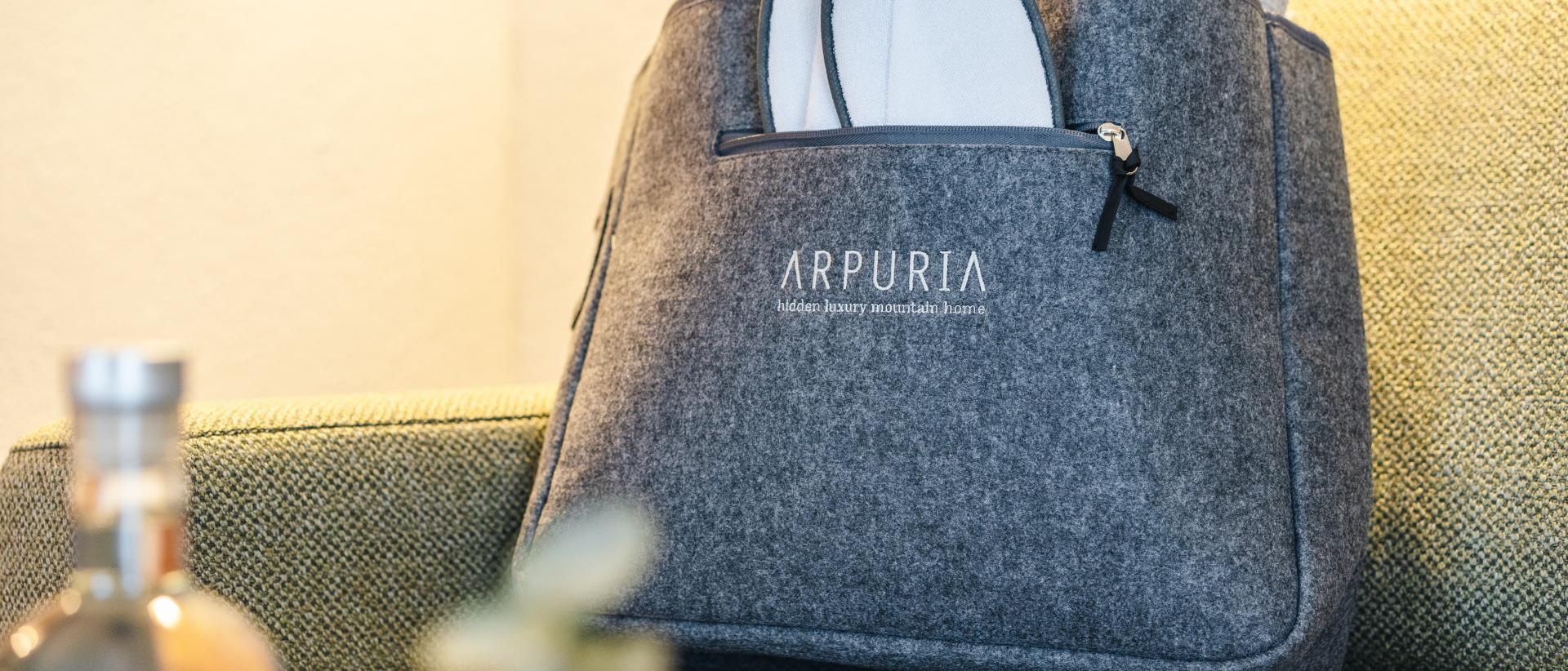 Filztasche des Hotel Arpuria mit weißen Hausschuhen auf einem Sofa