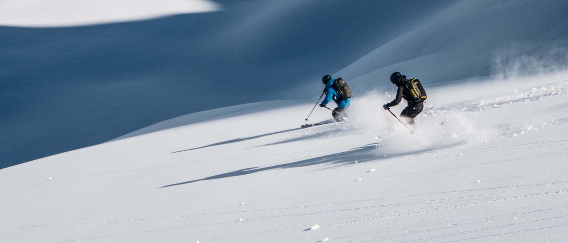 Two skiers skiing on fresh powder snow near Hotel Aurora