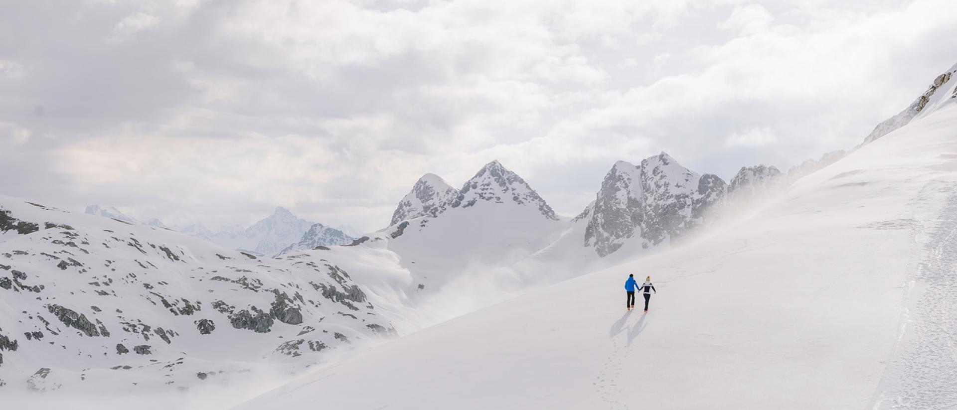 Zwei Personen wandern im Schnee mit Bergen im Hintergrund Hotel Aurora