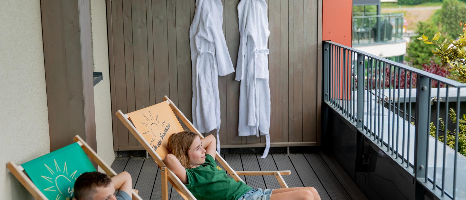 Kinder entspannen auf Balkon im Pfalzblick Wald Spa Resort mit Bademänteln im Hintergrund
