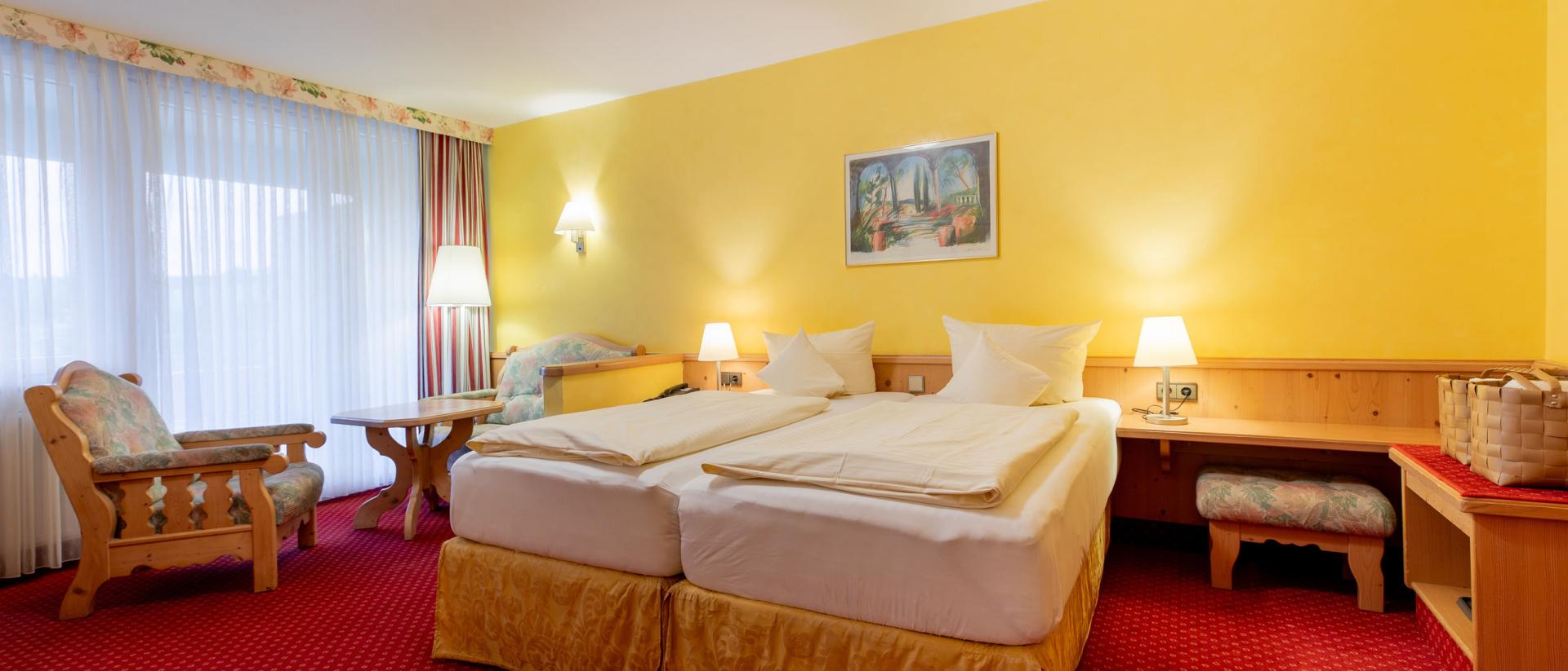Gemütliches Doppelzimmer im Pfalzblick Wald Spa Resort mit Sitzbereich und gelben Wänden