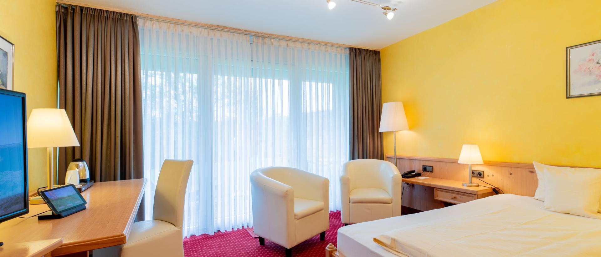 Gemütliches Hotelzimmer im Pfalzblick Wald Spa Resort mit gelben Wänden und rotem Teppich