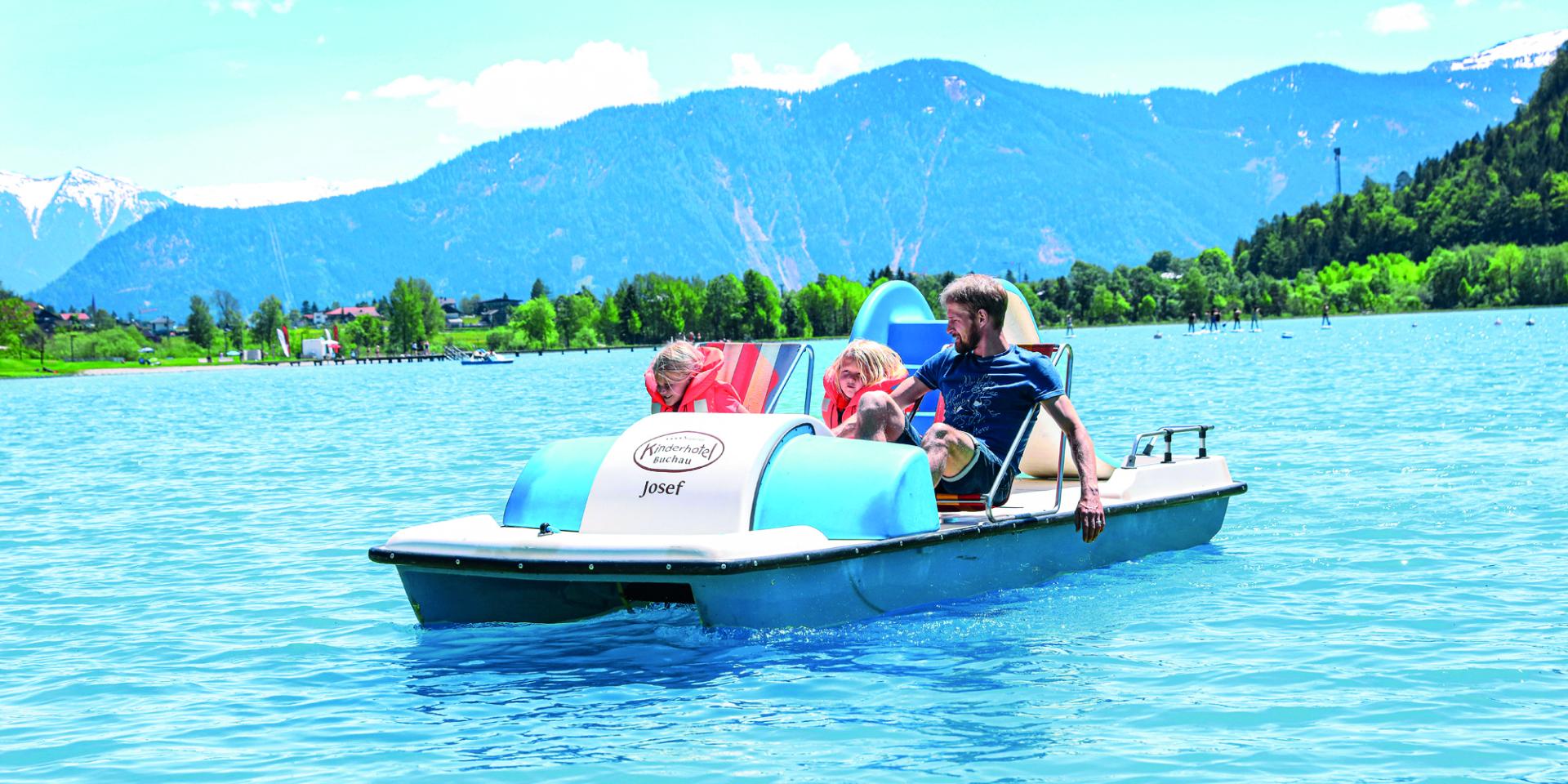 Family pedal boating on the lake at Familienresort Buchau with mountains in the background
