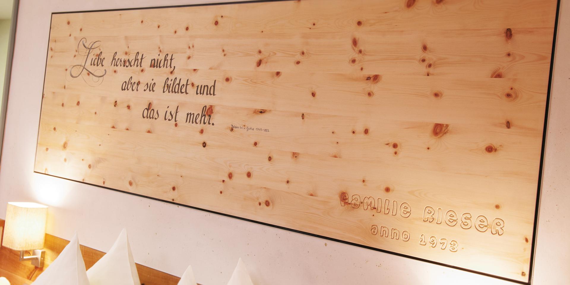 Holzdeko im Familienresort Buchau mit dem Zitat Liebe herrscht nicht, aber sie bildet.
