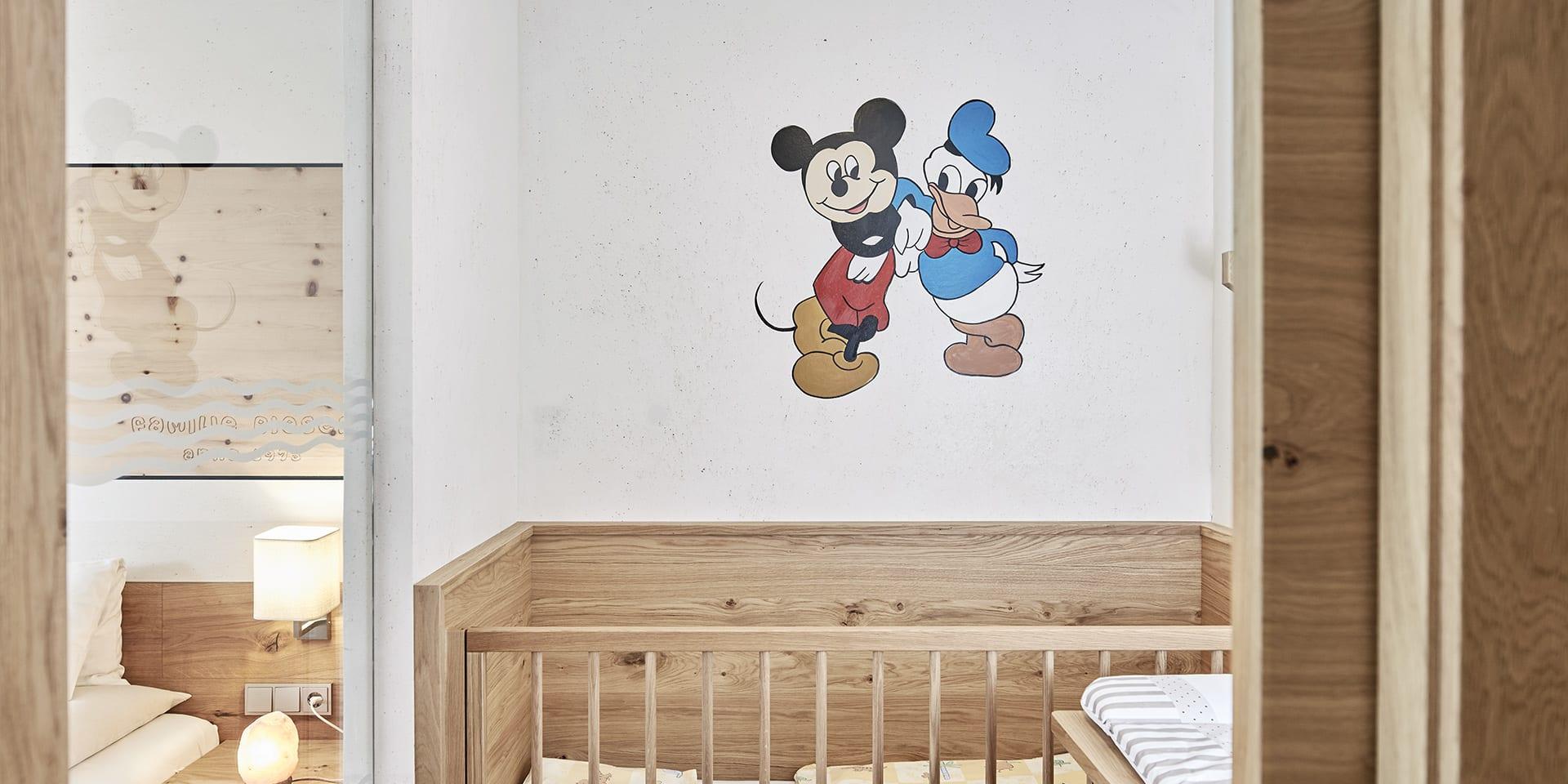 Kinderzimmer mit Gitterbett und Disney-Wandbild im Familienresort Buchau