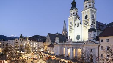 Laurena: Weihnachtsmarkt mit beleuchteter Kirche mit zwei Türmen in der Dämmerung