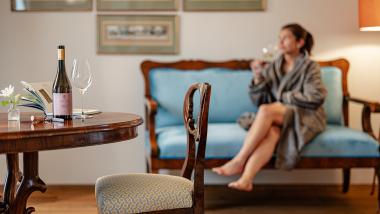 Flasche Castel Sallegg und Weinglas auf einem Tisch neben einer Frau auf dem Sofa