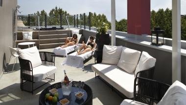 Terrazza sul tetto dell'Q Hotel con lettini, divani da giardino e due persone che prendono il sole