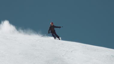 Der Greil Skifahrer fährt schnell einen schneebedeckten Hang hinunter vor klarem Himmel