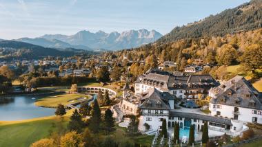 Schlosshotel Kitzbühel beside a lake, with autumn-colored mountains in the background