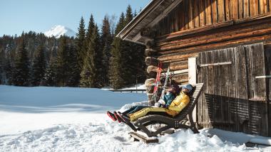 Gäste entspannen im Schnee vor einer Almhütte beim Biohotel Leutascherhof